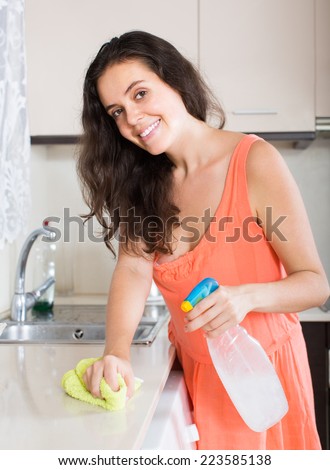 Smiling young housewife cleaning furniture in kitchen