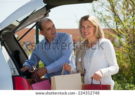 Happy mature couple staying with purchases near opened boot