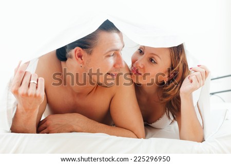 Loving middle-aged guy and woman  together under sheet on bed