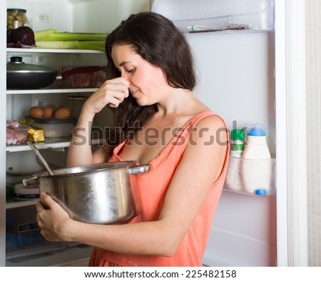 Brunette  woman  holding her nose because of bad smell near fridge at home