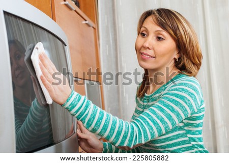 woman in green cleaning TV with rag at home