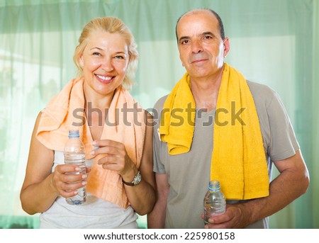 Active elderly spouses with bottles of water  smiling after morning exercises