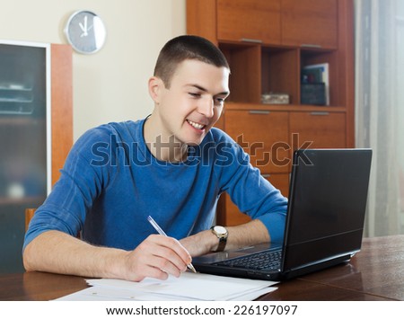 Smiling guy  staring financial documents at table in home interior
