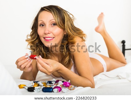 Happy smiling blonde woman eating candy in bed at home
