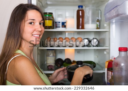 Young smiling woman with saucepan near refrigerator at home