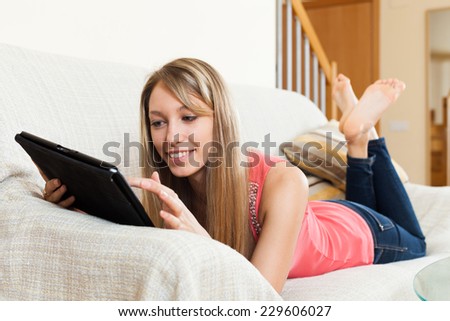 Smiling attractive blond girl laying on sofa with tablet pc computer