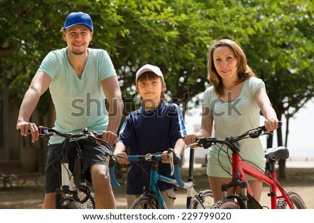 Active happy couple with teenager son staying in the street with bicycles