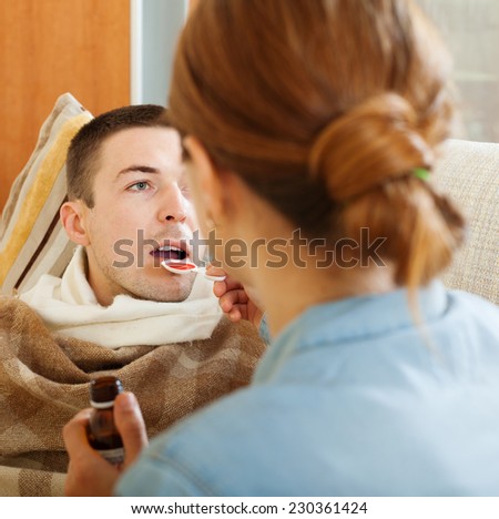 caring woman giving cough syrup to unwell man at home