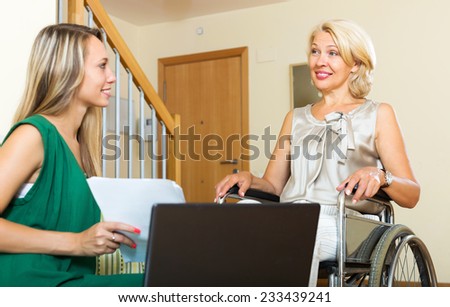 Friendly insurance agent and smiling disabled woman on chair indoor