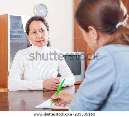 Sad mature woman filling questionnaire for employee with paper at table