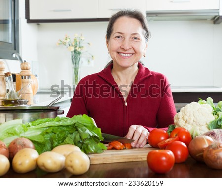 Mature woman with cutting tomato in home kitchen