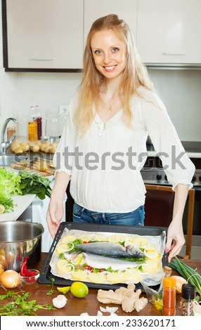 Positive housewife cooking full fish with potato in sheet pan at home kitchen