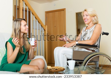 Female friend visiting disabled woman on chair indoor