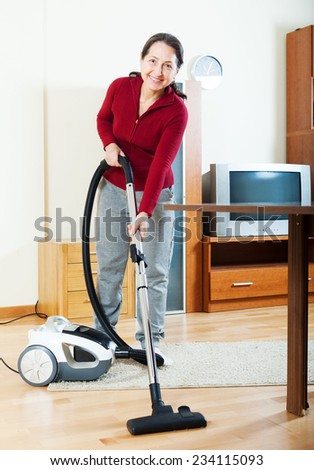 Happy mature woman with vacuum cleaner on parquet