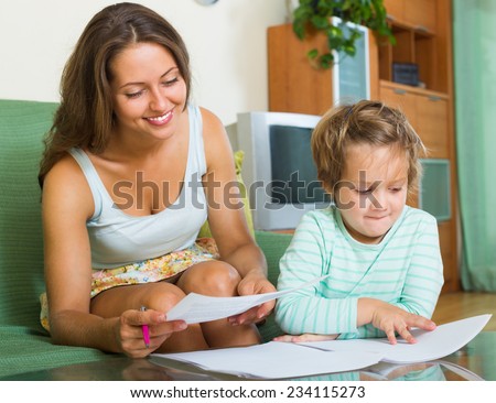 Cheerful woman and daughter signing application form for kindergarten indoor