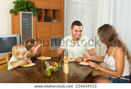 Young smiling parents with children having lunch with spaghetti at home together. Focus on man