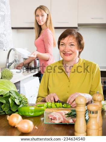 Smiling elderly mother with adult daughter cooking at kitchen