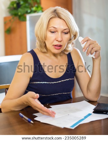 Serios mature woman filling in financial documents at table in home interior