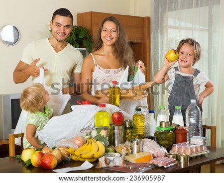 smiling family of four with bags of food at home