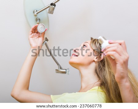 Happy young blonde woman changing light bulbs