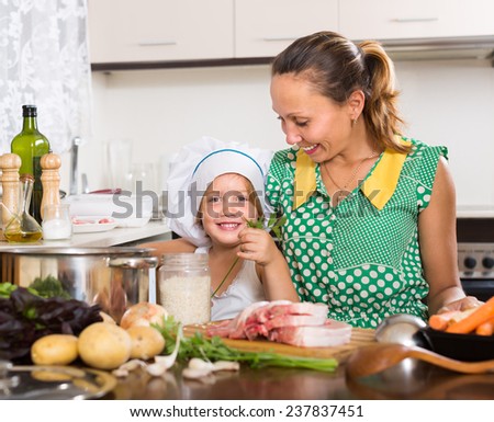 Smiling mother with little daughter in cook hat cooking soup at kitchen