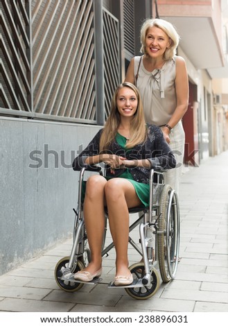 Friendly social worker and disabled girl on chair at stroll. Focus on girl