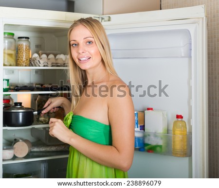 Smiling blonde woman with saucepan near refrigerator at home