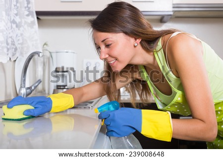 young  happy woman in apron cleaning kitchen sink at home