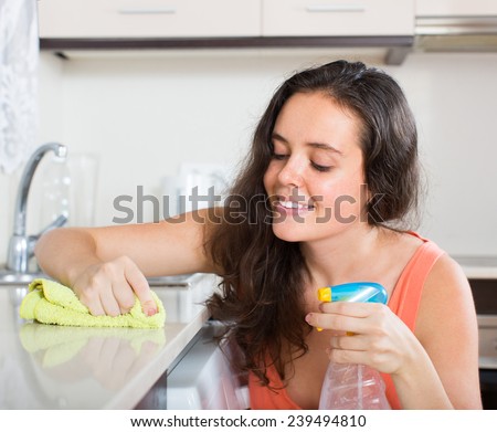 Happy young housewife cleaning furniture in kitchen