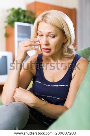 Sad and lonely mature woman 60 years old sitting on couch at home