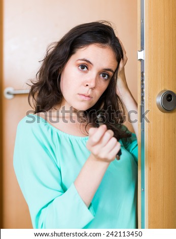Sad young brunette woman looking at broken lock of outer door