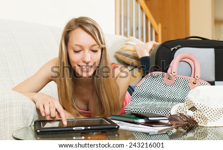 Smiling young woman with  suitcase searching for travel destination on digital tablet in home interior