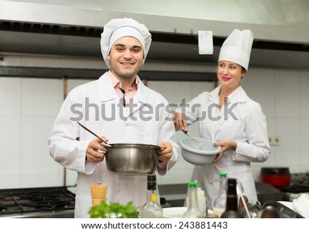Two professional cooks working at restaurant kitchen. Focus on man