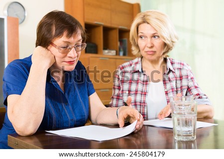 Two sad elderly women reading documents at table