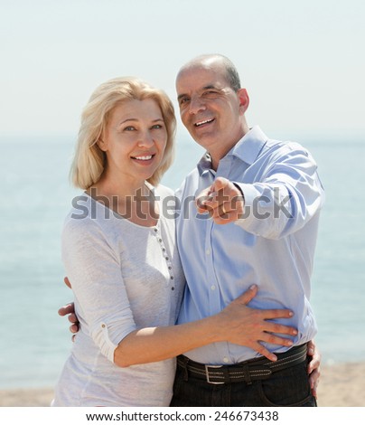 Happy elderly man showing something hand an elderly woman on the beach