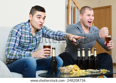 Adult happy friends sitting at table with beer and commenting sport tv channel