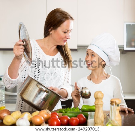 beautiful little girl and her mother cook soup together in the kitchen