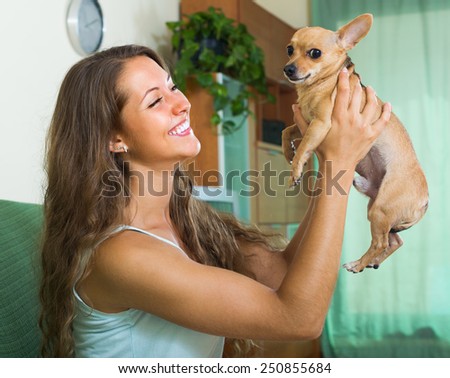 Happy smiling young female holding Russkiy Toy Terrier indoor