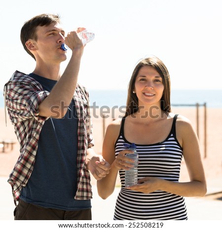 Thirsty young couple drinking water from bottle at sunny day