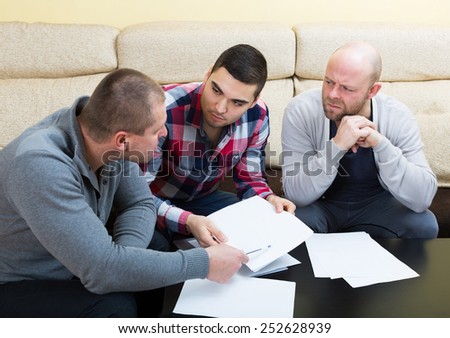 Three men with documents discussing financial issues