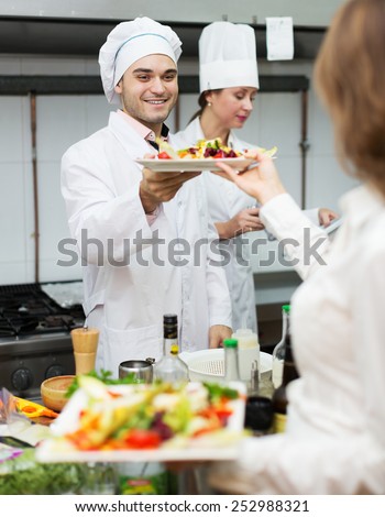Team of chefs and young beautiful waiter in the restaurant kitchen