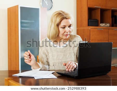 serious mature woman with notebook and documents at table in office