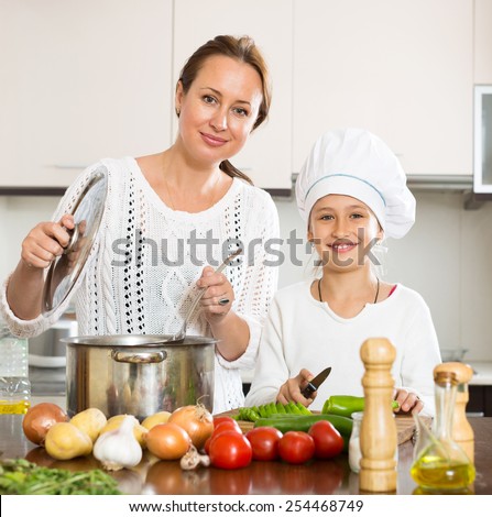 Happy little girl and her mother cook soup together in the kitchen