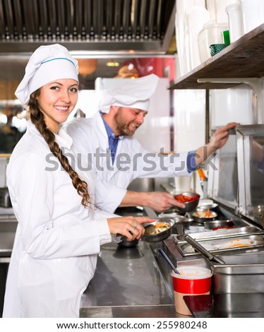 Smiling professional chef and cook  working at take-away restaurant kitchen