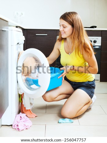 Smiling long-haired woman using washing machine at home