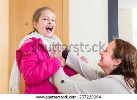 Family portrait of mother helping cheerful little girl to dress up. Focus on girl