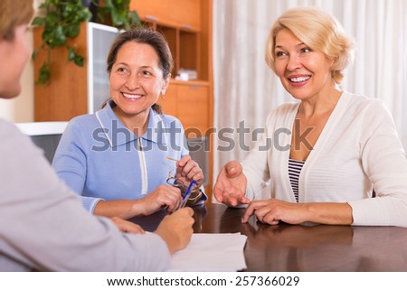 Smiling positive senior ladies signing documents at bank with agent