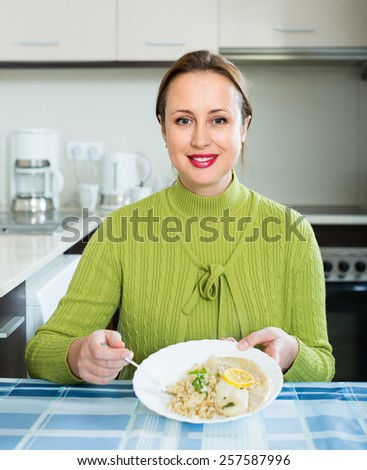 Smiling woman tasting fried fish with rice at home
