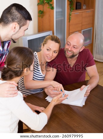 Young spouses sitting with documents and asking happy friends for advice