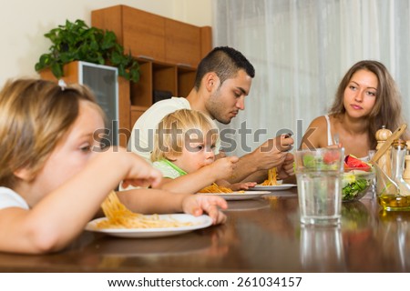 Young family with two little children eating with spaghetti at table. Focus on girl